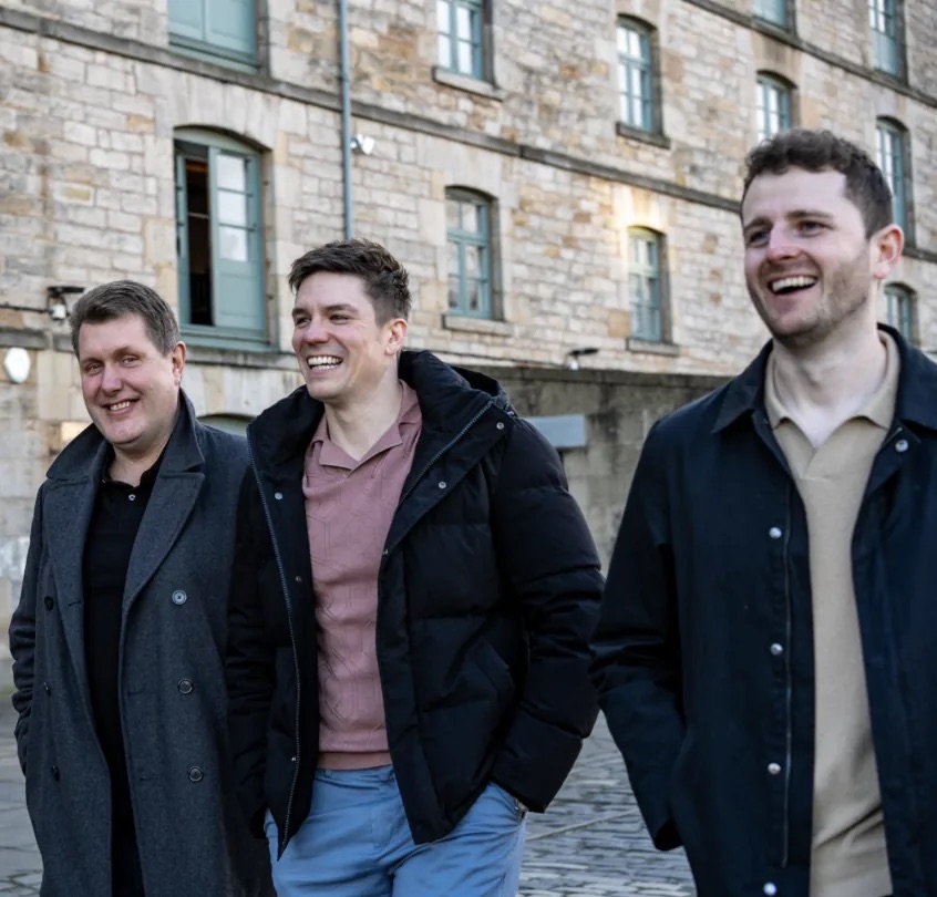 Three ePass team members walking together past a stone-built office in Edinburgh